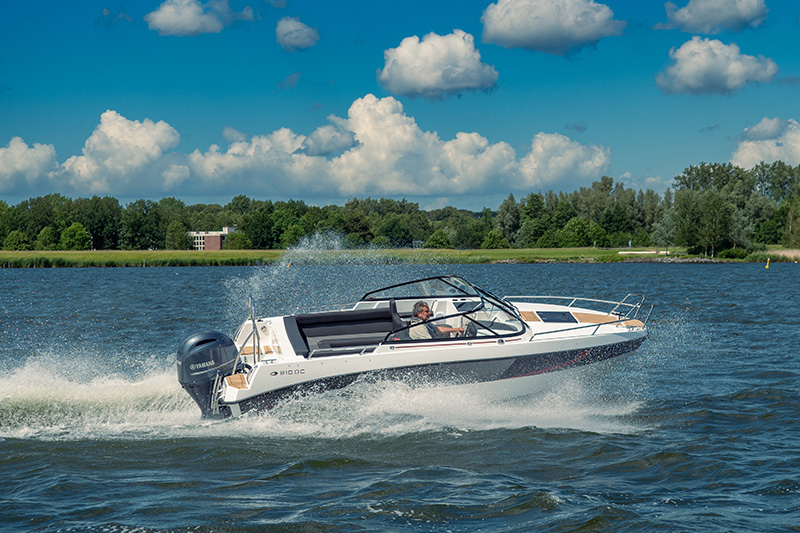 De AMT 210 DC in plané op onrustig water, met de wal op de achtergrond.