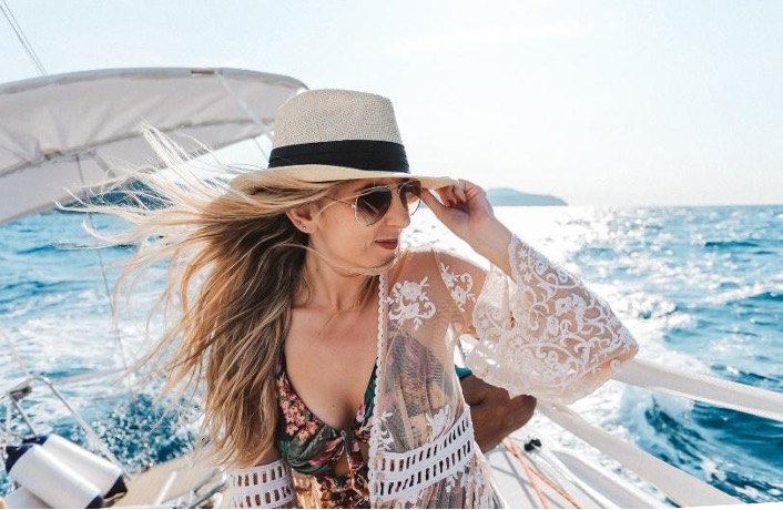 Vrouw op zeilboot in zomerse kleding en zonnehoed
