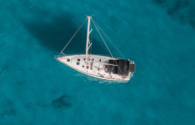 A birds-eye view of a sailboat floating in clear blue water