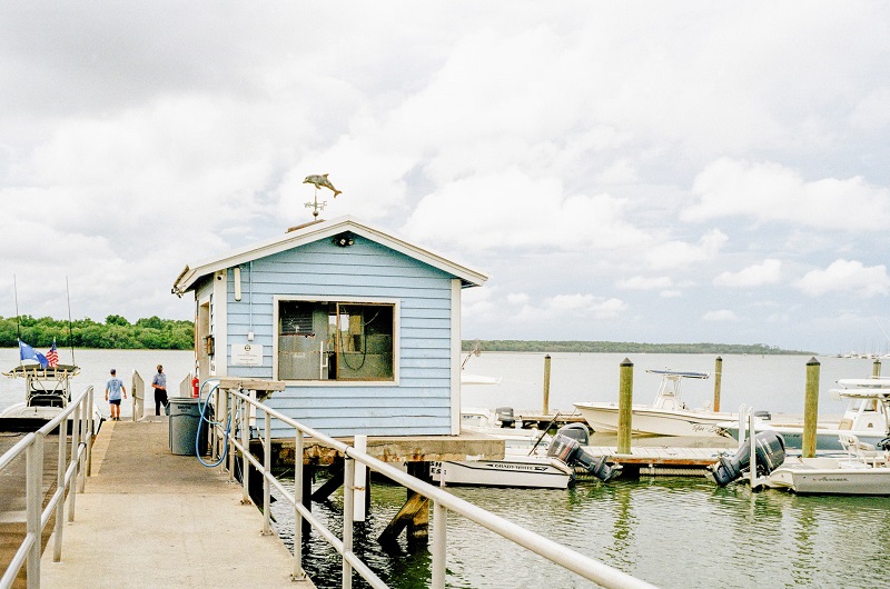 Een blauw houten botenhuis op een steiger naast aangelegde boten.