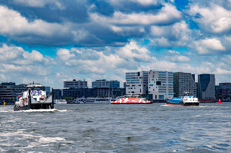 Het IJ in Amsterdam met veel bootverkeer op het water en gebouwen op de achtergrond.