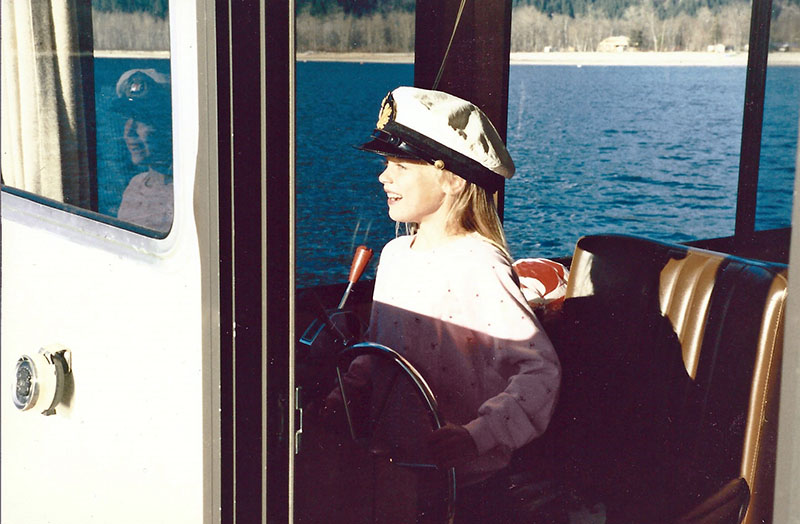 Une petite fille avec une casquette de capitaine à la barre d'un bateau.