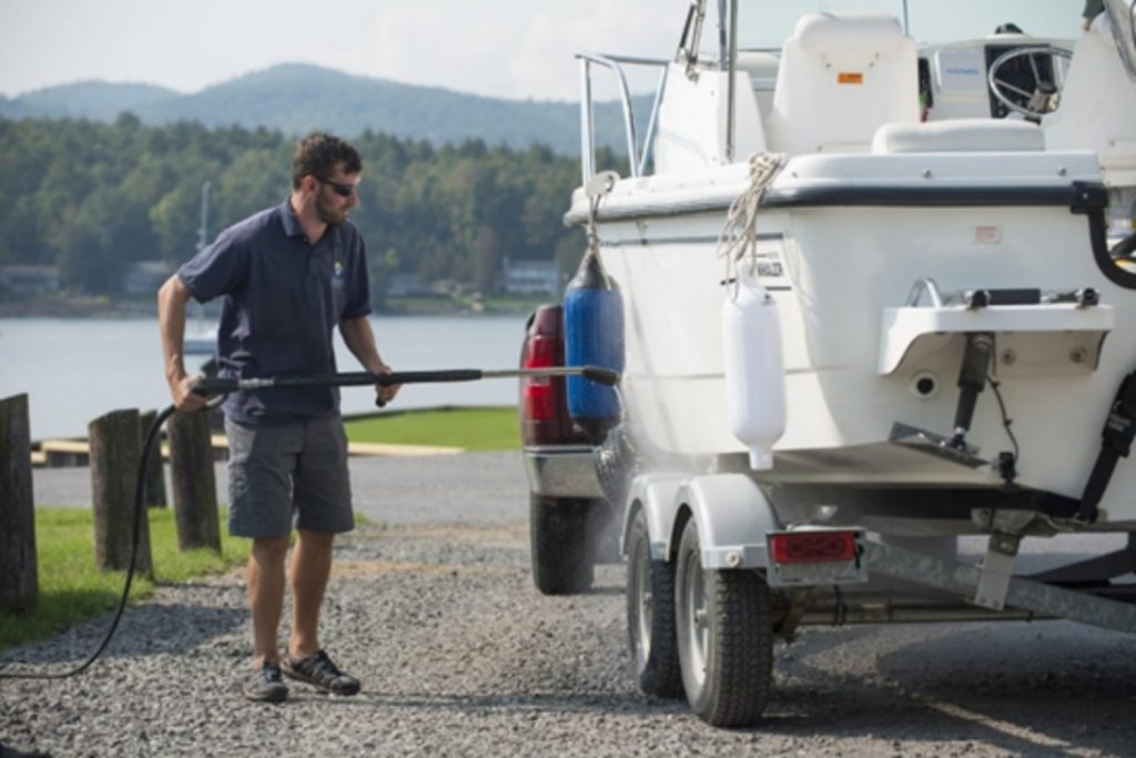 Man cleaning boat on land with a power washer machine