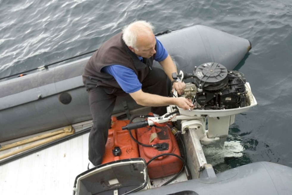 A man sitting on a boat fixes the boat engine with a metal tool