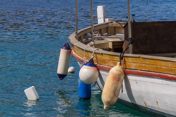 Worn-looking fenders of different sizes hanging from side of boat, with fuel can floating nearby.