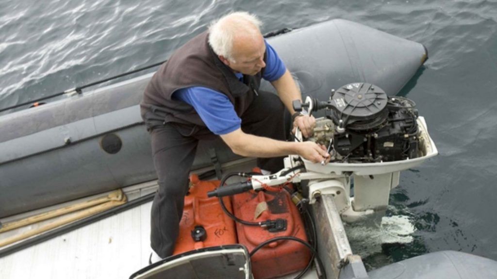 Un homme assis sur un bateau répare le moteur à l’aide d’un outil métallique