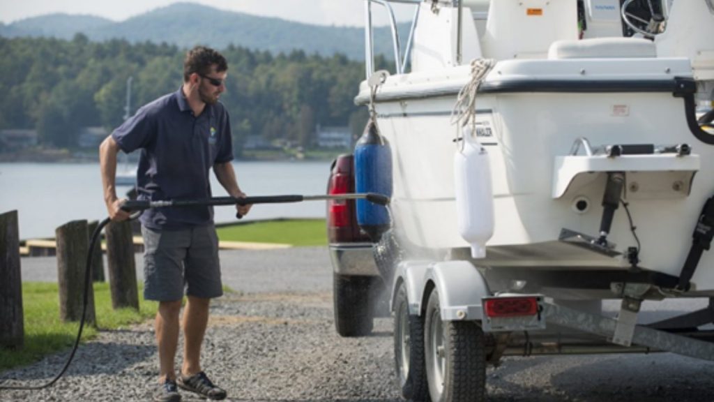 Un homme nettoie son bateau à terre avec un nettoyeur à haute-pression