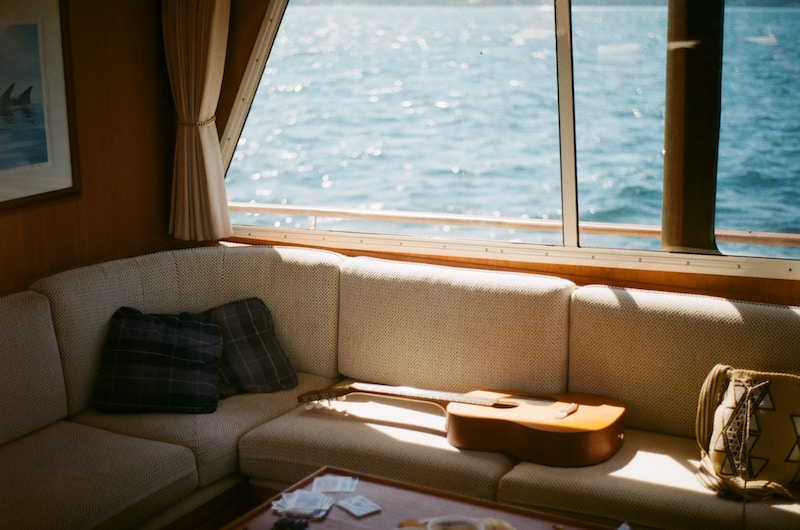 Une guitare posée sur une banquette sous une fenêtre avec vue sur l’eau bleue.