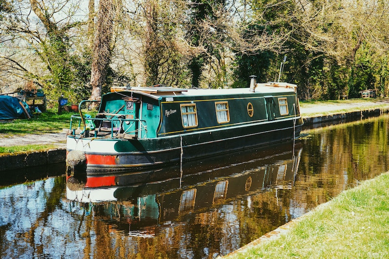 A green canal boat on a canal in autumn sunshine