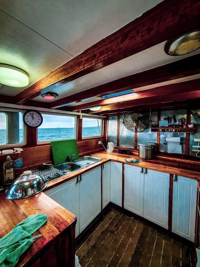 Een kombuis met houten aanrecht en witgeschilderde keukenkastjes. Door de scheepsramen is de zee te zien.