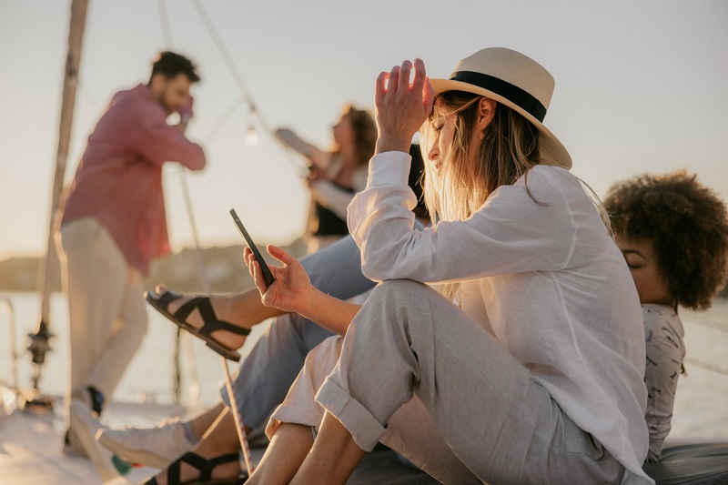 Een groep jonge mensen op een boot praat met elkaar en gebruikt hun telefoons