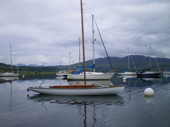 Small yacht anchored in a harbour with mountains in the background