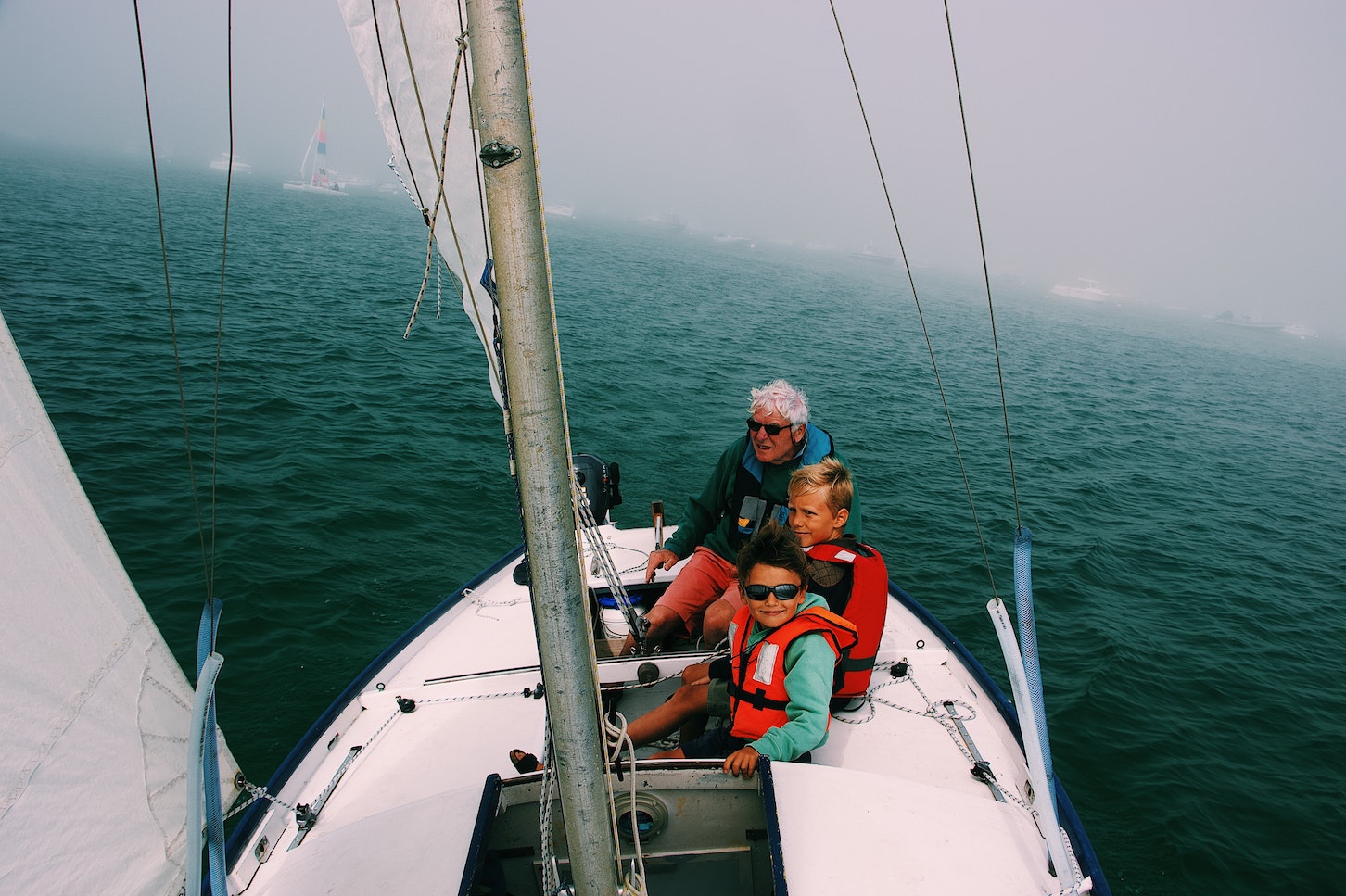a grandfather and two grandchildren wearing lifejackets on a sailing boat