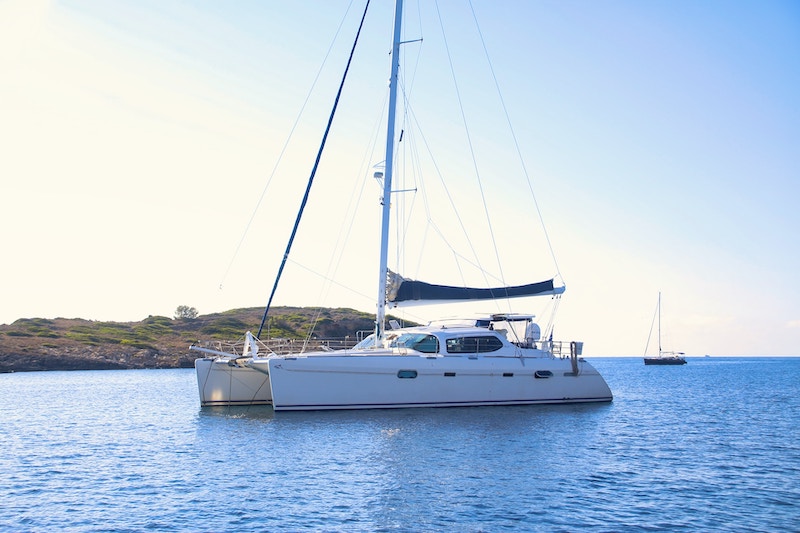 Un catamaran blanc dans une baie méditerranéenne. Lumière chaude du soir. 