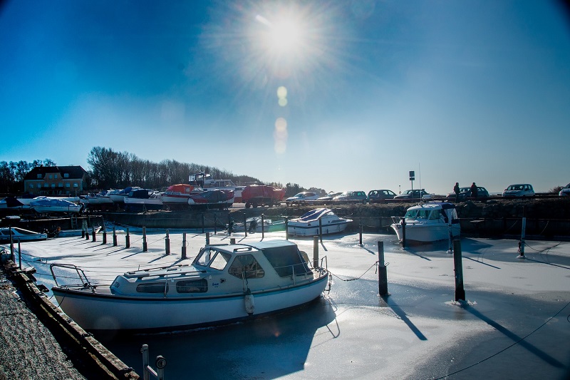 Bijna lege haven met ijs om de boten heen en blauwe lucht 