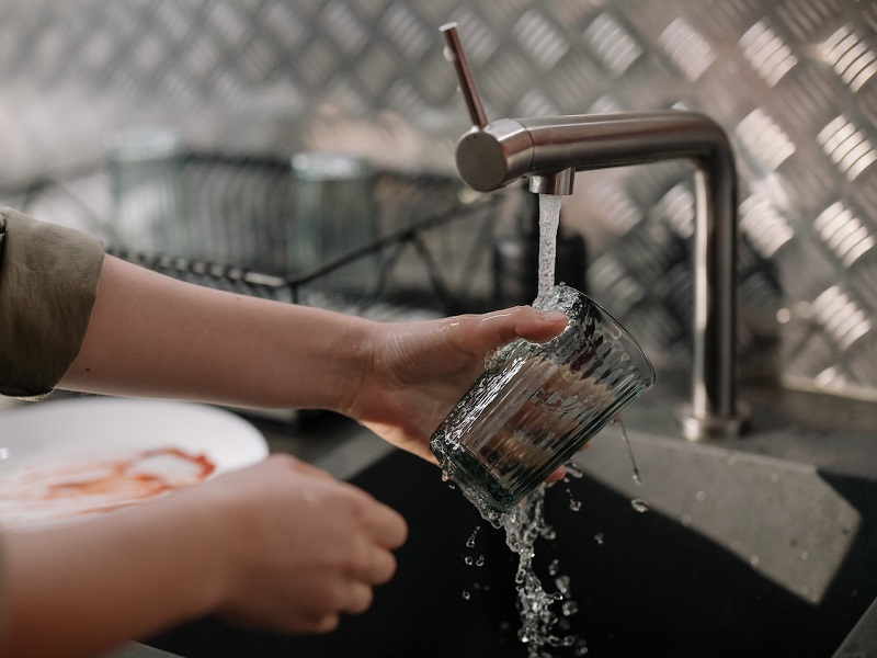 Lavage d’un verre à la main sous un robinet, avec des plats sales sur le côté.