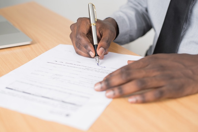 Hände einer Person, die ein amtliches Dokument an einem Schreibtisch unterschreibt.