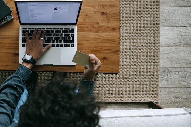 Man seen from above using laptop while holding bank card in one hand.