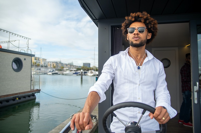 Junger Mann mit Sonnenbrille, der ein Boot steuert.