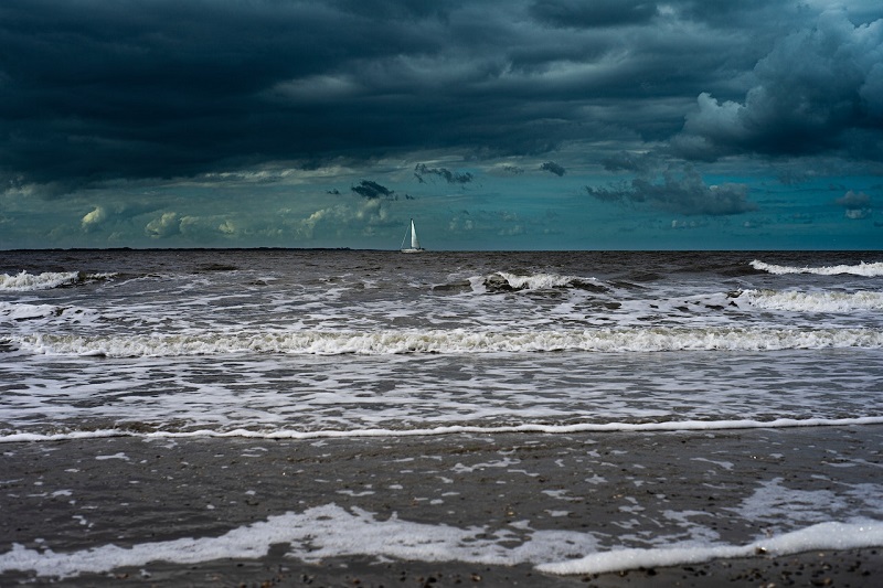 Sailboat far in the distance with storm clouds overhead.