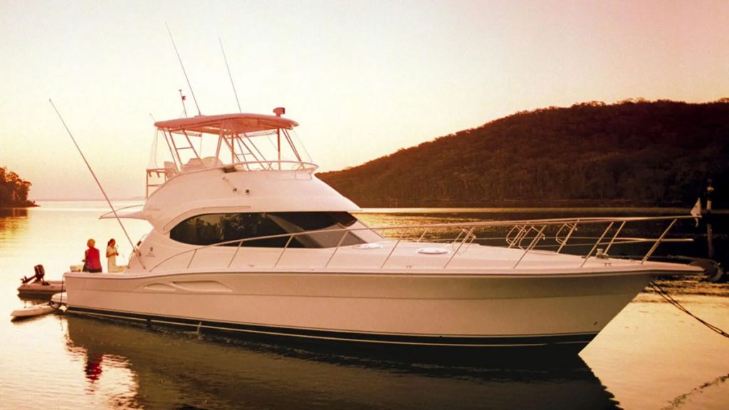 Large, modern powerboat with people aboard, anchored in bay during golden hour.