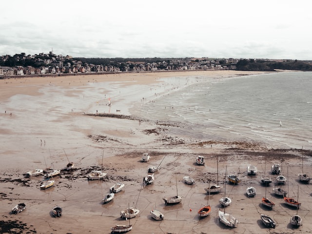 Blick auf einen Strand bei Niedrigwasser mit vielen Booten, die auf dem Sand liegen. 