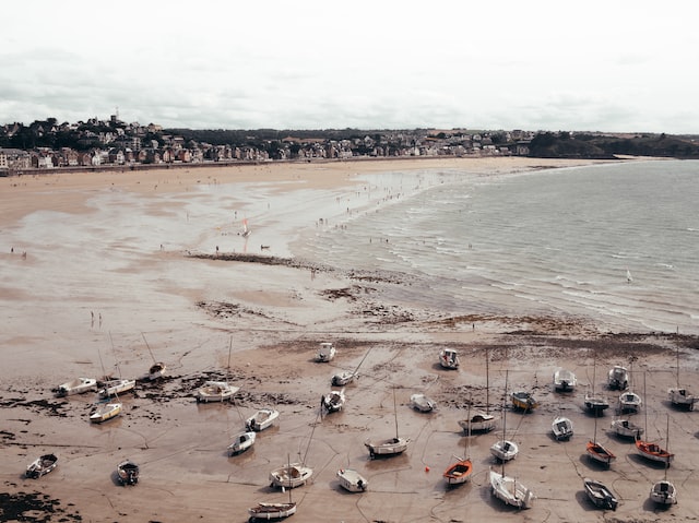 View of a beach at low tide with many boats resting on the sand.