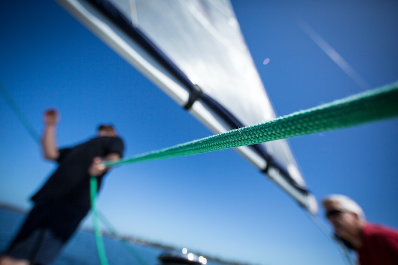 Close-up van een man die een lijn vasthoudt terwijl hij naar de zeilen van een boot kijkt. 