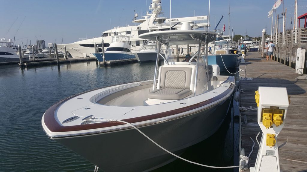 Small powerboat docked at harbour, with larger boats in background.
